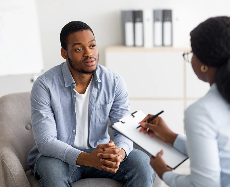 Unhappy-young-black-man-having-session-with-professional-psychologist-at-mental-health-clinic